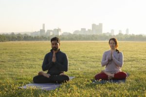 Person meditating outdoors near calm water, surrounded by greenery, embodying holistic health and mindfulness practices.